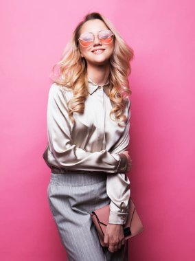 Bluz giyen genç güzel sarışın kadın, pantolon ve güneş gözlüğü bir çanta tutar