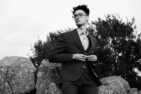 Fashionable young man sitting on the rocks near the sea — Stock Photo, Image