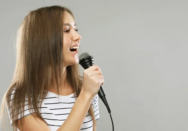 Девушка-модель певица с микрофоном на светло-сером фоне — стоковое фото