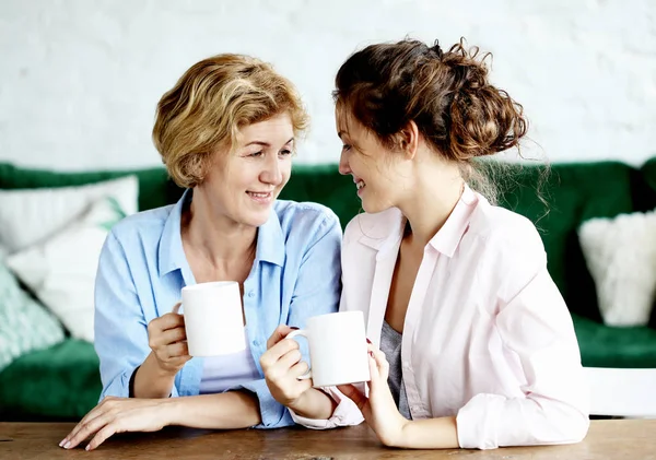 Дві красиві жінки мати і дочка сидять на дивані вдома. Вони п'ють каву, чай. . — стокове фото