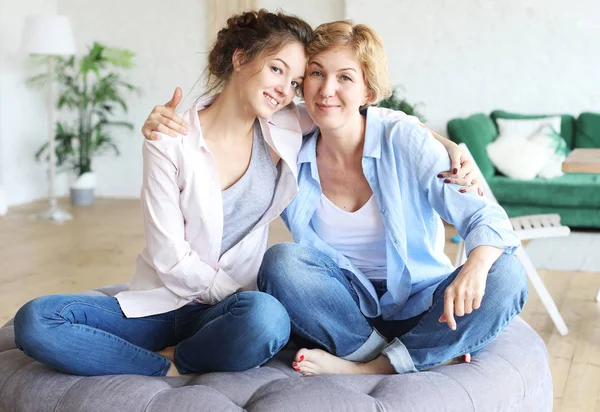 Hermosa mamá mayor y su hija adulta están abrazando, mirando a la cámara y sonriendo. En casa. —  Fotos de Stock