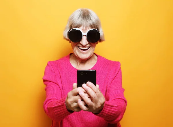 Old grandmother is talking to her grandchildren by phone, smiling and greeting them. — Stock Photo, Image