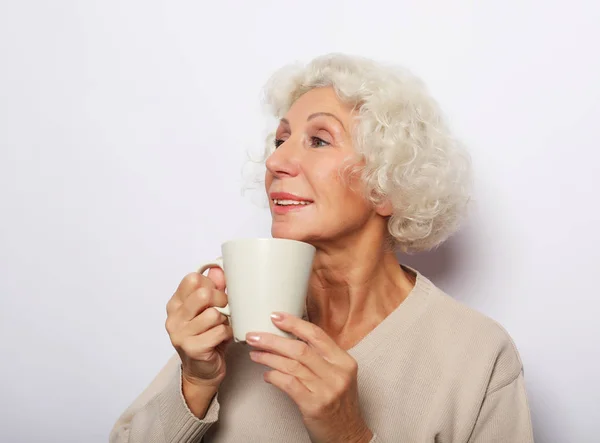 old excited lady smiling laughing, holding cup drinking coffee, tea, over white background
