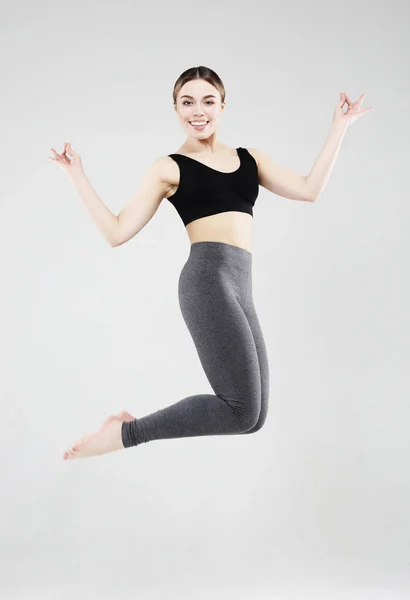 Spor, Fitness ve insan kavramı: güzel genç kadın spor elbise giymiş gri arka plan üzerinden atlama — Stok fotoğraf
