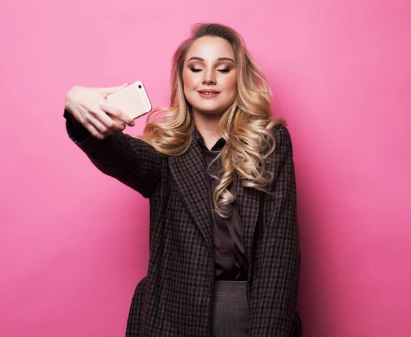 Szőke lány fotózás teszi önarckép okostelefon felett rózsaszín háttér — Stock Fotó
