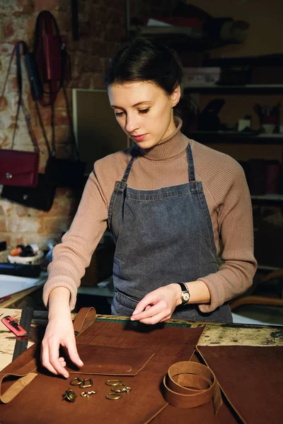 Jeune femme brune travaille dans un studio de fabrication de sacs, découpe les détails — Photo