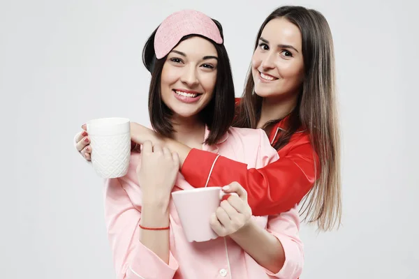 Estilo de vida, la amistad y el concepto de la gente - dos hermosas chicas vestidas en pijama abrazando y sonriendo —  Fotos de Stock