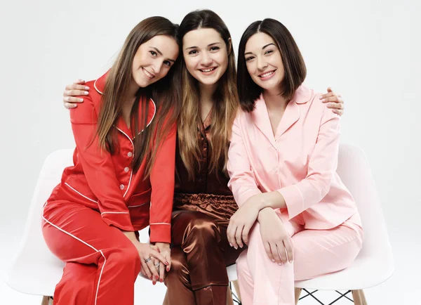 Tre flickvänner klädda i pyjamas sitta på stolar och posera för kameran. — Stockfoto