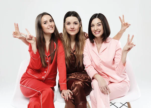 Tre flickvänner klädda i pyjamas sitta på stolar och posera för kameran. — Stockfoto