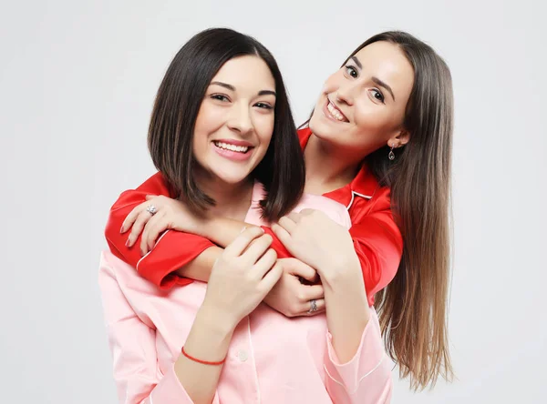 Estilo de vida, la amistad y el concepto de la gente - dos hermosas chicas vestidas en pijama abrazando y sonriendo —  Fotos de Stock