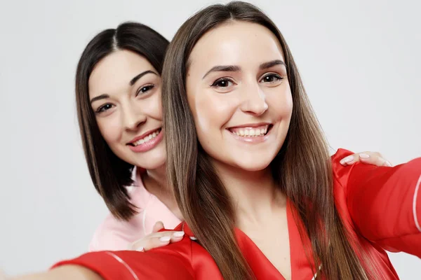 Életmód és az emberek koncepciója: két gyönyörű lány pizsamába öltözve ölelkezve és szelfiket készítve — Stock Fotó