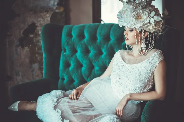 A noiva nova bonita que veste o vestido branco e a grinalda das flores senta-se em uma cadeira. Palácio de luxo . — Fotografia de Stock