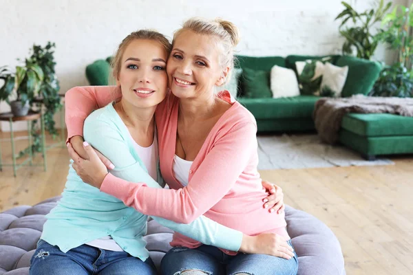 Hermosa mamá mayor y su hija adulta están abrazando, mirando a la cámara y sonriendo. En casa. —  Fotos de Stock
