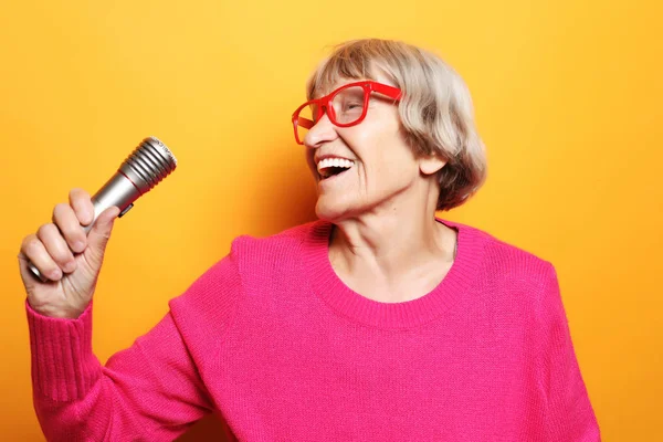 Divertida abuela sostiene el soporte del micrófono y canta aislado sobre fondo amarillo vivo — Foto de Stock