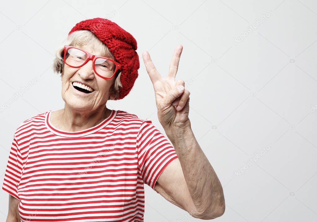 Old woman laugh and showing peace or victory signat camera. Emotion and feelings. Portrait of expressive grandmother.