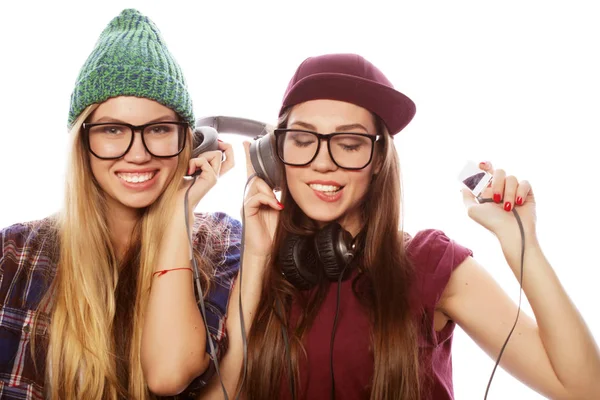 Dos hermosas chicas vestidas como hipsters escuchan música juntas, usan auriculares —  Fotos de Stock