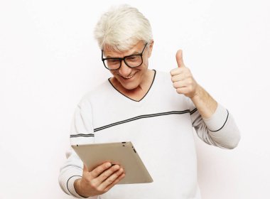 Gri saçlı yaşlı adam ailesiyle tablet ile iletişim kuruyor.