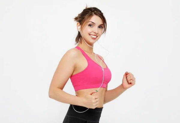 Retrato de una mujer fitness sonriente con auriculares trabajando aislados sobre fondo blanco — Foto de Stock