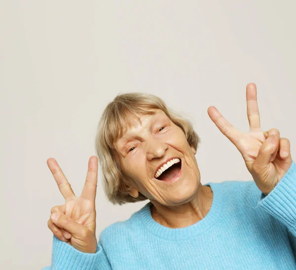 Mulher velha rir e mostrando paz ou vitória sinalizar câmera. Emoção e sentimentos. Retrato de avó expressiva. — Fotografia de Stock