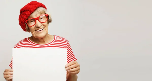 Portret szczęśliwej seniorki z pustą tablicą reklamową lub przestrzenią do kopiowania, na jasnoszarym tle — Zdjęcie stockowe