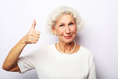 Yaşam tarzı, duygu ve insan konsepti: Yaşlı mutlu kadın başparmağını kaldırıyor ve kameraya bakıyor