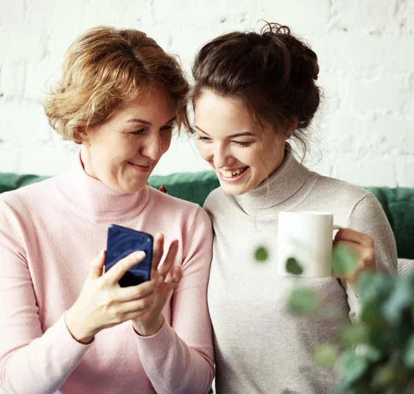 Сім'я, люди і технології. У віці жінка і її доросла дочка використовують смартфон вдома . — стокове фото