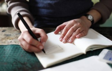 Genç kadın dikiş atölyesinde deftere el yapımı konsept yazıyor.