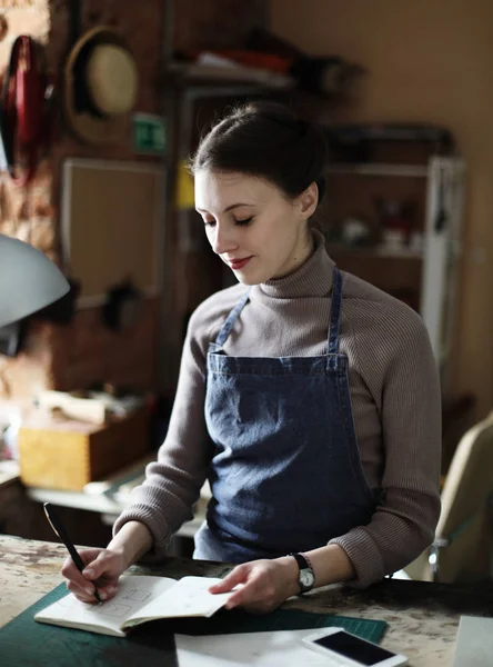 young woman writes to notebook in sewing workshop, handmade concept