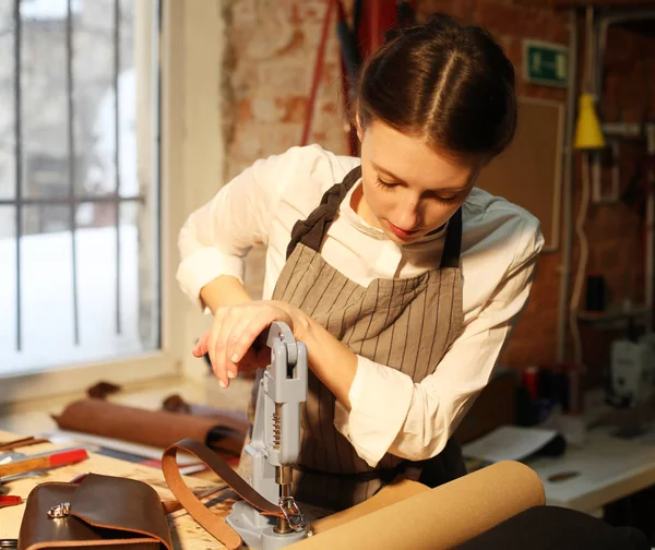 Νεαρή μελαχρινή γυναίκα εργάζεται σε ένα στούντιο κατασκευής τσαντών, κόβει τις λεπτομέρειες — Φωτογραφία Αρχείου