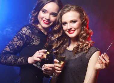 İki güzel genç kadın siyah elbise ile şarap bardakları ve yangın ışıltı.