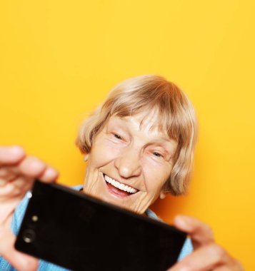 yaşam tarzı, tehnology ve insanlar kavramı: Büyükanne mavi kazaklı gülümsüyor ve bir selfie alır