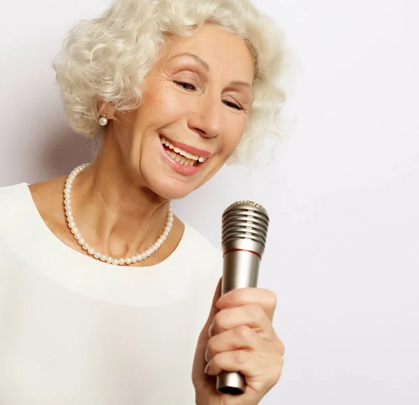 Estilo de vida y el concepto de la gente: Retrato de la encantadora abuela moderna sostiene el soporte del micrófono y canta — Foto de Stock