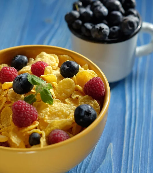 Cornflakes with berries raspberries and blueberries on blue wooden background.