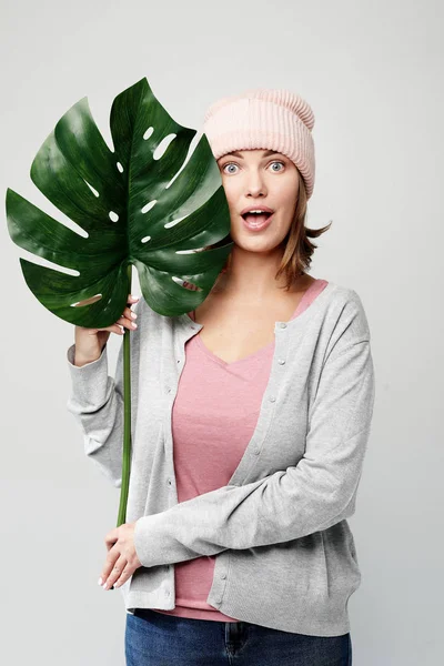 Молодая женщина держит лист большого тропического цветка и улыбается — стоковое фото