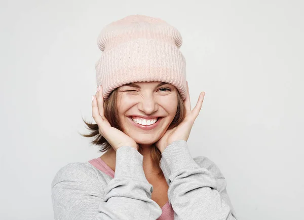 Funny young woman in a pink beanie hat makes faces and poses over light grey background — Stock Photo, Image