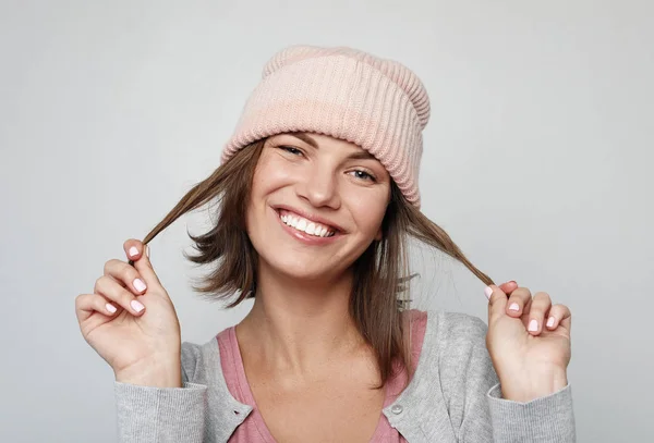 Mujer joven divertida en un sombrero de gorro rosa hace caras y posa sobre fondo gris claro — Foto de Stock