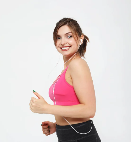 Πορτρέτο μιας χαμογελαστής γυναίκας γυμναστικής στα ακουστικά που εργάζονται απομονωμένη σε λευκό φόντο — Φωτογραφία Αρχείου