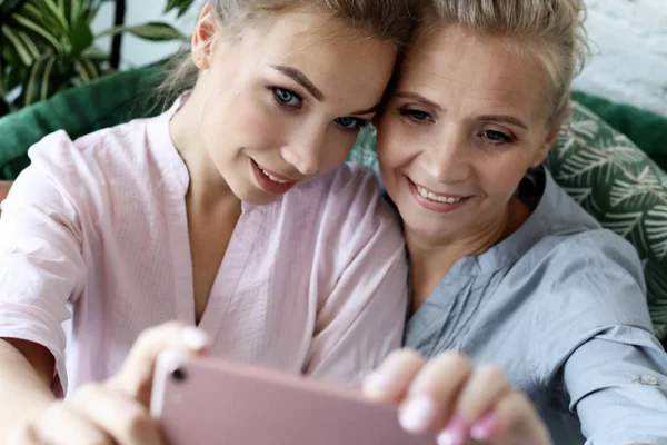 Πορτρέτο της όμορφης ώριμης μητέρας και της κόρης της κάνοντας μια selfie χρησιμοποιώντας έξυπνο τηλέφωνο και χαμογελώντας, σπίτι και ευτυχισμένη. — Φωτογραφία Αρχείου