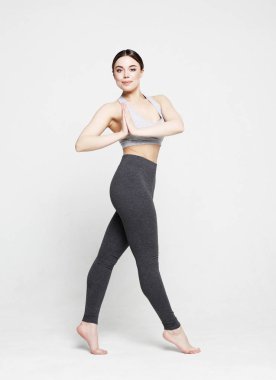 Spor kıyafetleri içinde beyaz bir arka planda poz veren genç ve güzel bir kadın.