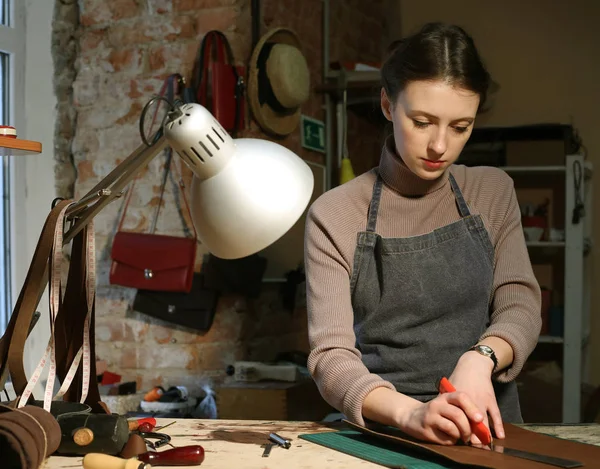 Jeune femme brune travaille dans un studio de fabrication de sacs, découpe les détails — Photo