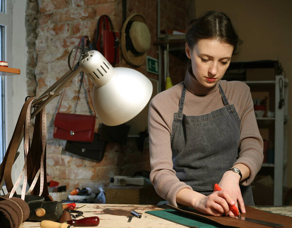 young brunette woman works in a bag making studio, cuts out details