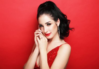 Yaşam tarzı, parti ve insan konsepti - gece elbisesi içindeki güzel esmer kadın flörtçü ve kırmızı arka planda şakacı