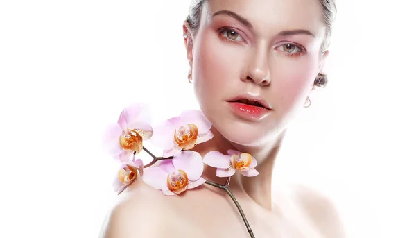 Pembe tonlarda parlak makyajlı genç bir kadın elinde beyaz bir arka planda çekim yapan bir orkide tutuyor. — Stok fotoğraf