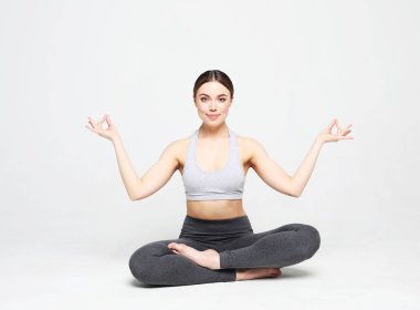 Yoga yapan, spor giyinen, beyaz arka planda çekim yapan genç bir kadın.
