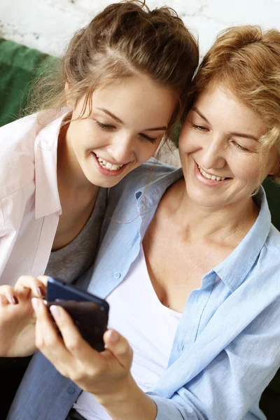 Семья, люди и технологии. Пожилая женщина и ее взрослая дочь используют смартфон дома. — стоковое фото