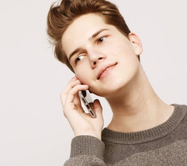 Tişörtlü gülümseyen adam gri arka planda akıllı telefonla konuşuyor.