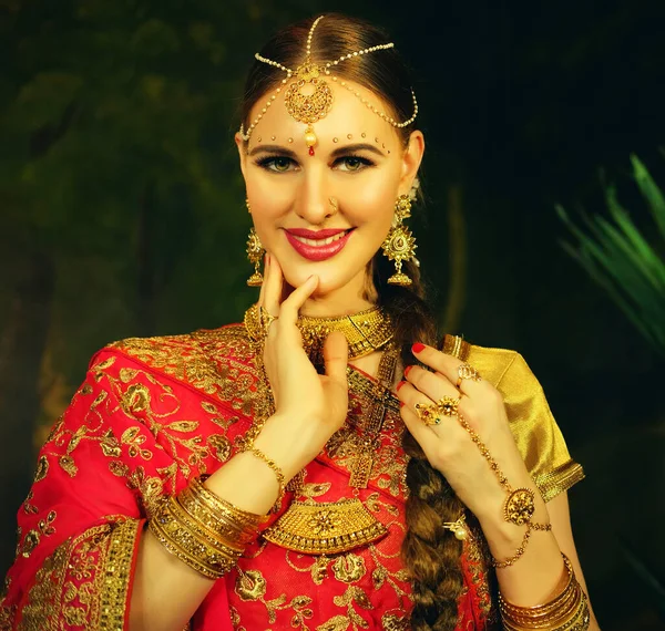 Portrait smiling of beautiful indian girl at home. Young woman model with golden jewelry set .