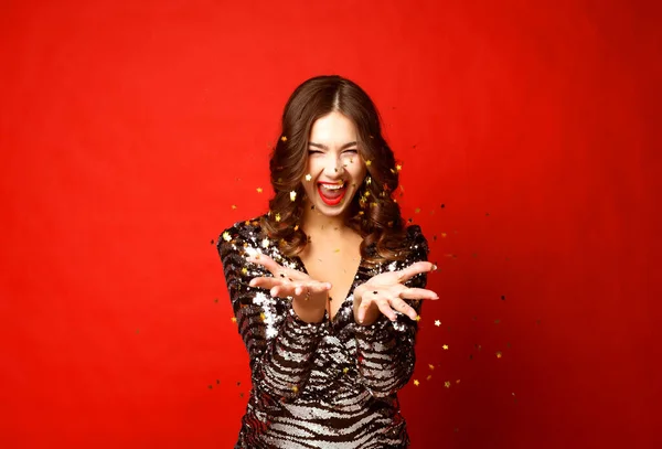 Beautiful girl wearing evening dress standing standing under confetti rain over red background — Stock Photo, Image