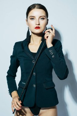 Siyah takım elbiseli, kırbaçla poz veren güzel, genç bir kadın.