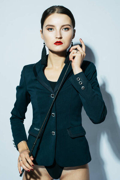 Красивая молодая женщина доминирует в черном костюме, позируя с кнутом
